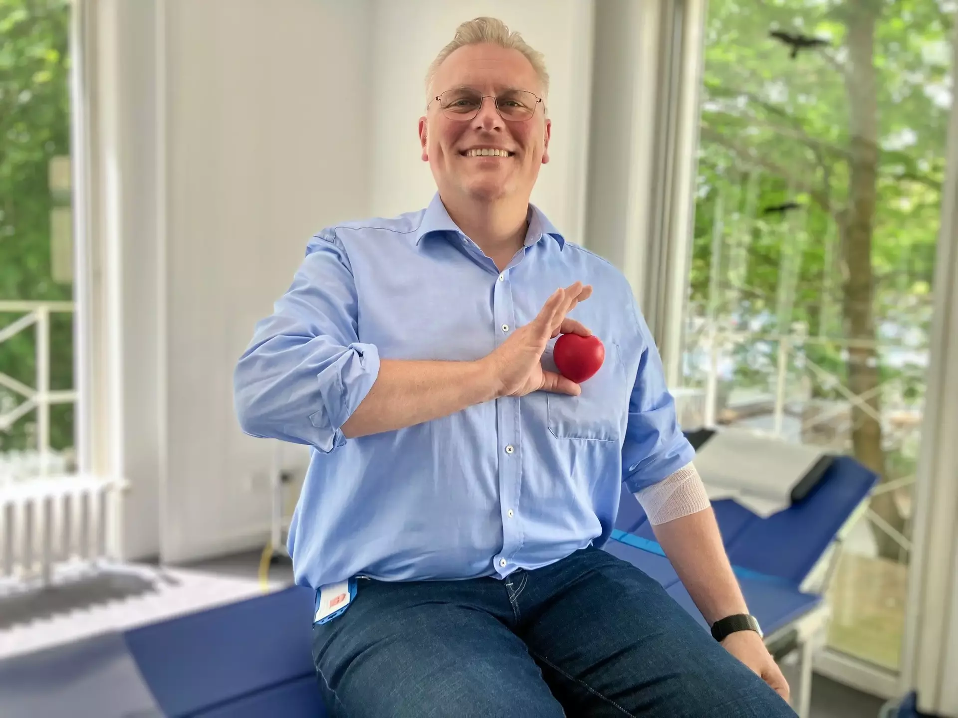Unser Personalleiter Florian sitzt nach der Blutspende lächelnd mit einem roten Herz-Stressball in der Hand.