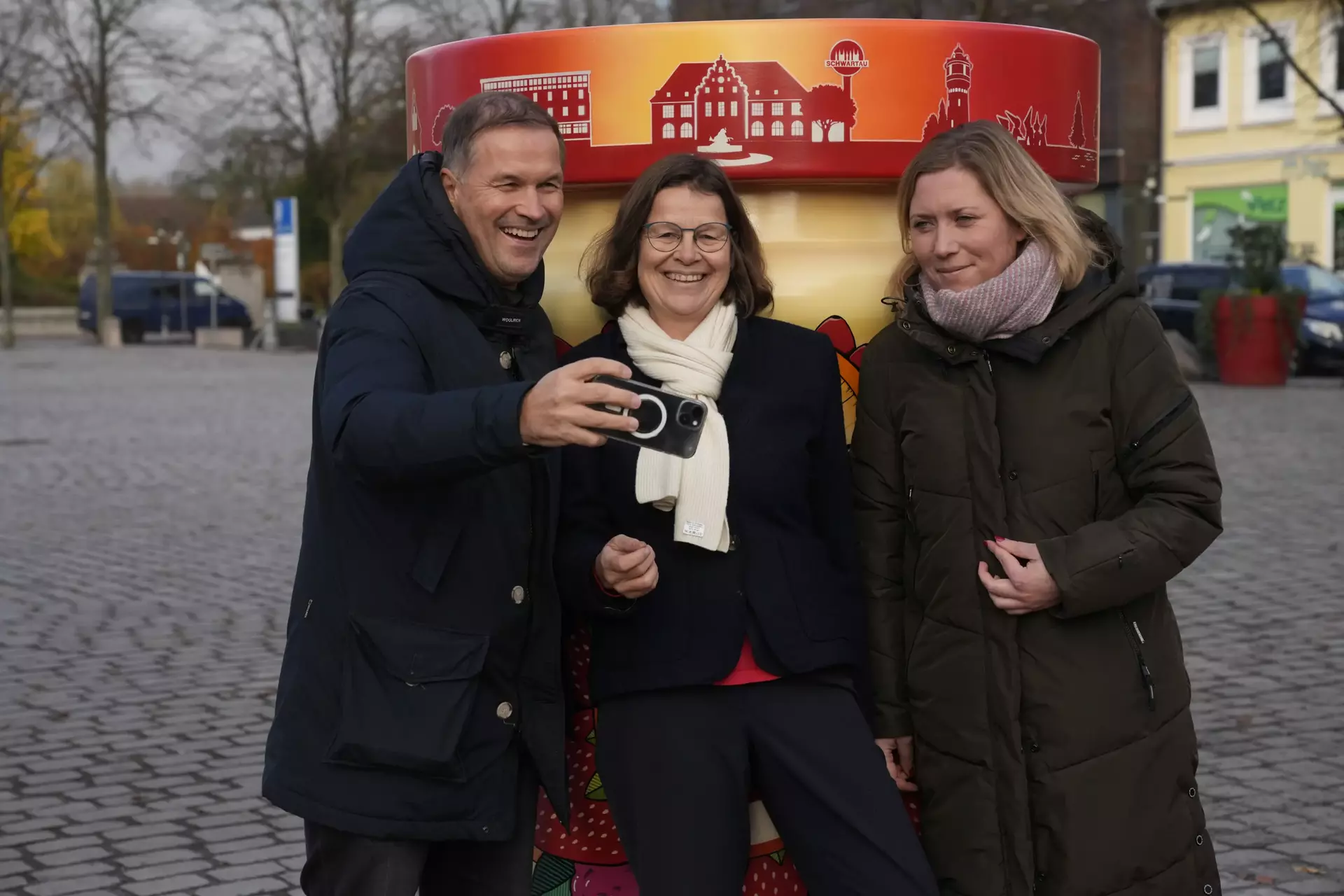 Links steht ein Mann, daneben zwei Frauen, die gemeinsam vor dem Fotopoint "Marmeladenstadt" das erste Selfie nach der Eröffnung machen.