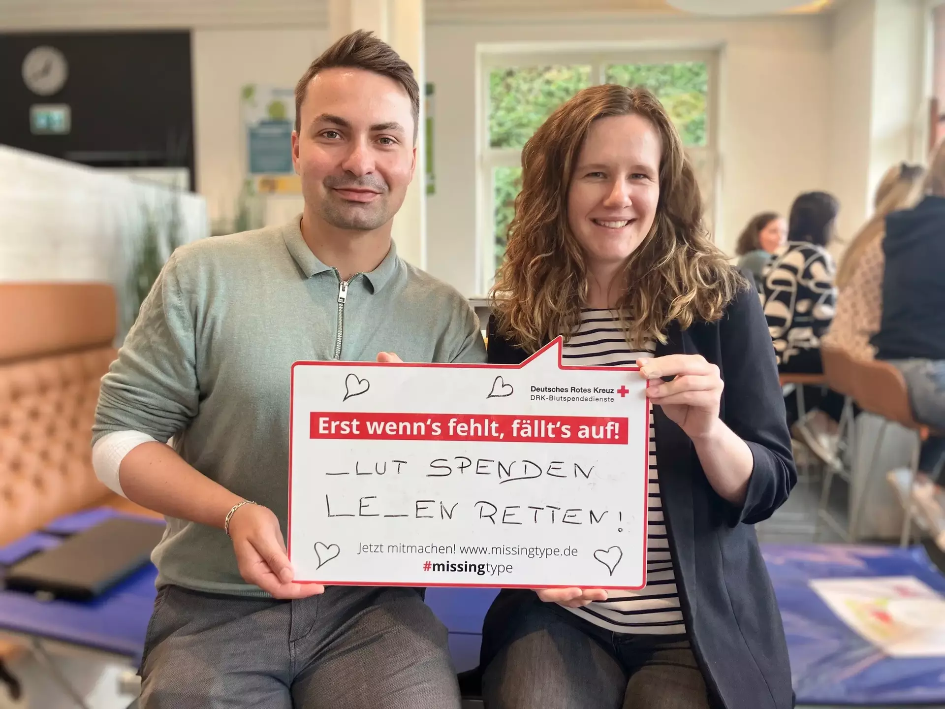 Hannes und Henrieke aus dem Marketing halten ein Schild mit der Aufschrift: ‚Erst wenn's fehlt, fällt's auf! _LUT SPENDEN LE_EN RETTEN! Jetzt mitmachen! www.missingtype.de #missingtype‘ – eine Aktion zur Blutspende, bei der bewusst Buchstaben weggelassen wurden, um auf ihre Bedeutung aufmerksam zu machen.