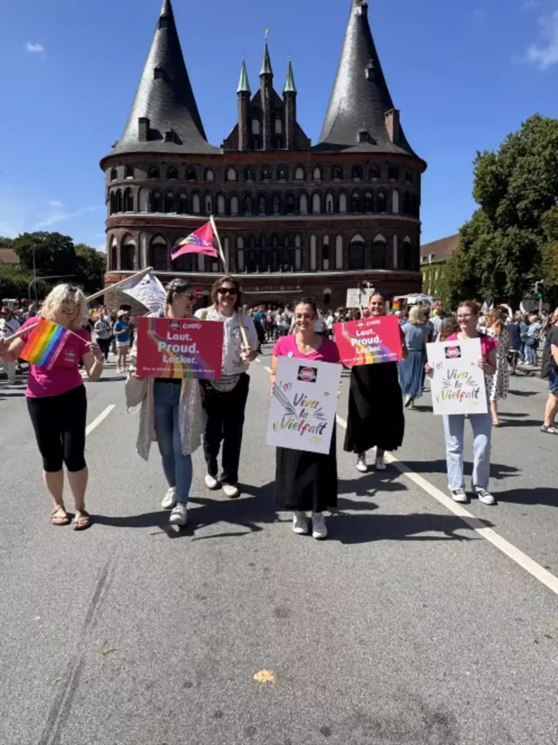 Personen aus Team Schwartau mit bunten Schildern vor dem Holstentor beim Lübecker CSD
