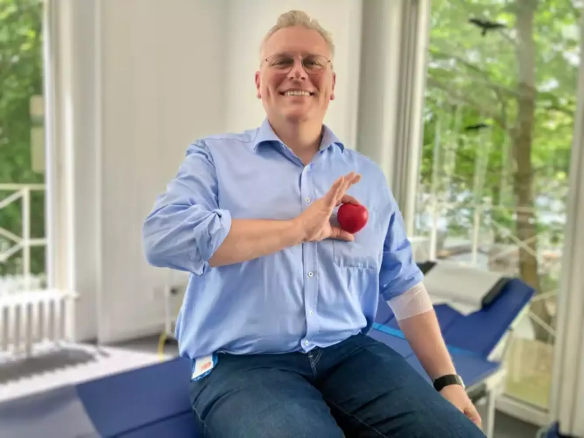 Unser Personalleiter Florian sitzt nach der Blutspende lächelnd mit einem roten Herz-Stressball in der Hand.
