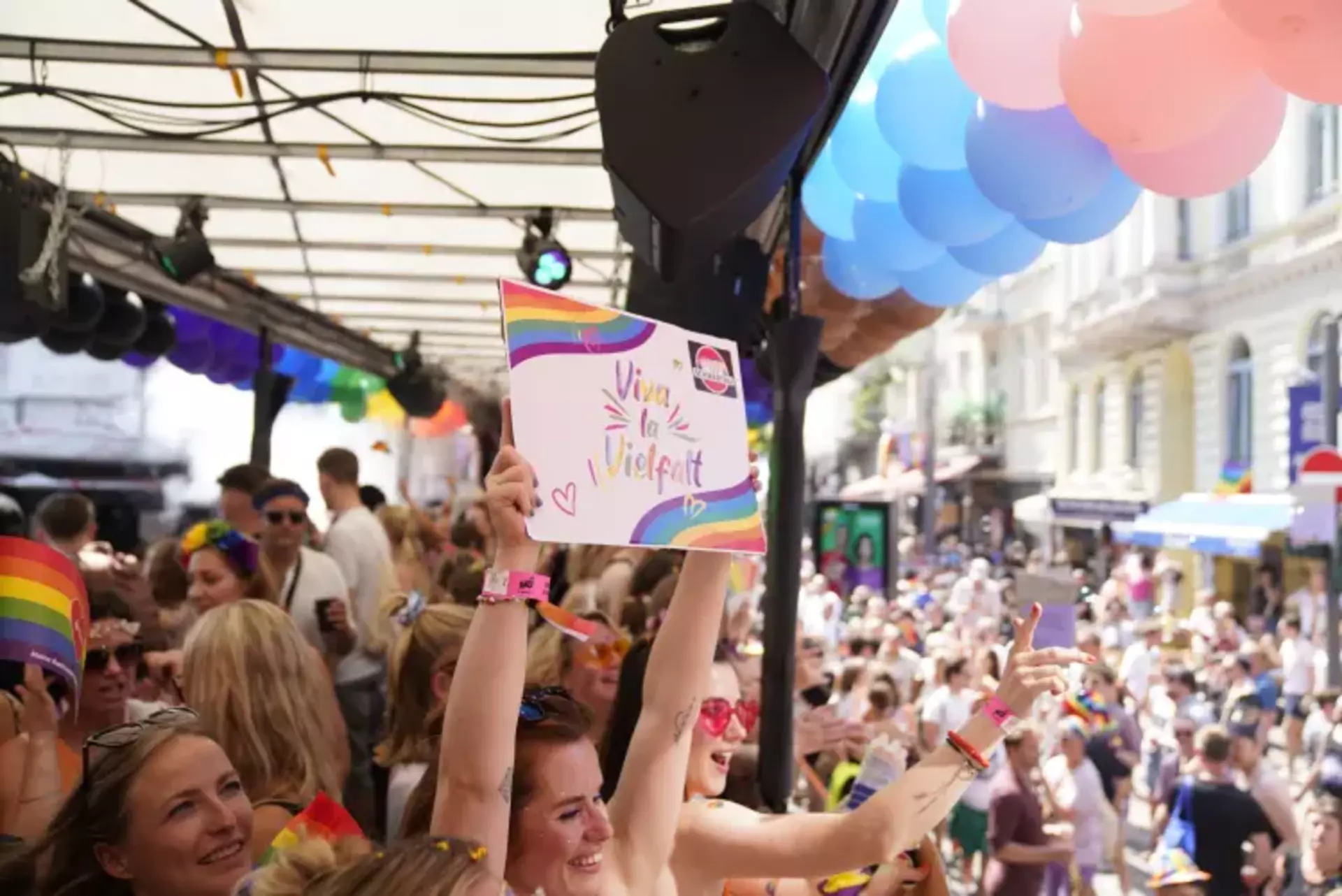 Junge Frau hält ein Schild mit "Viva la Vielfalt" Botschaft vom Truck beim CSD Hamburg, im Hintergrund sieht man die Pride-Parade