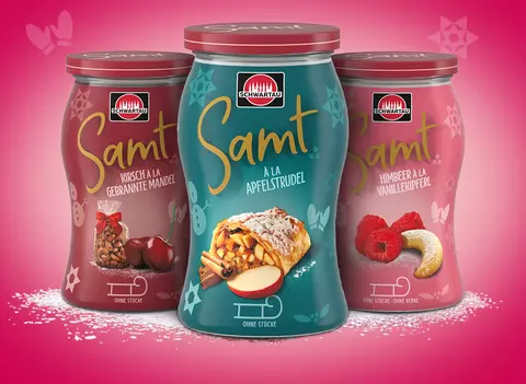 Drei Gläser der Schwartau Samt Winteredition mit den Sorten Kirsch à la gebrannte Mandel, Apfelstrudel und Himbeer à la Vanillekipferl. Die Fruchtaufstriche stehen vor einem pinken Hintergrund mit winterlichen Illustrationen und zeigen die jeweiligen Zutaten der Rezepturen.