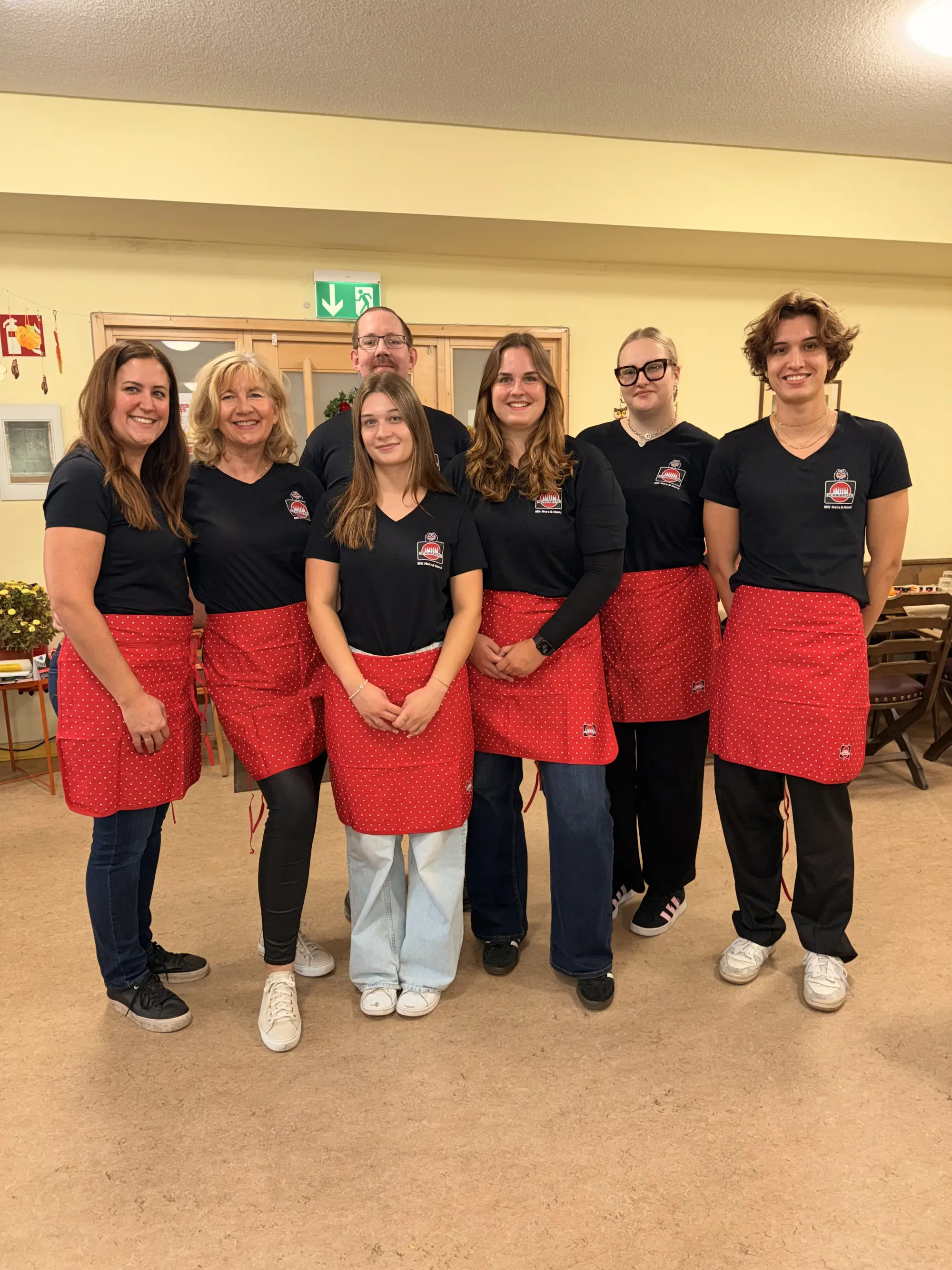 Gruppenfoto aller teilnehmenden Kolleg*innen, zu sehen sind sieben Personen unterschiedlichen Alters mit schwarzen Schwartau-T-Shirts und roten Kochschürzen.