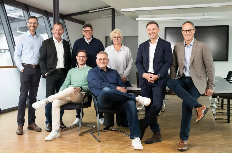 Acht Personen des Leadership Teams der Schwartauer Werke stehen und sitzen gemeinsam in einem hellen, modernen Besprechungsraum.